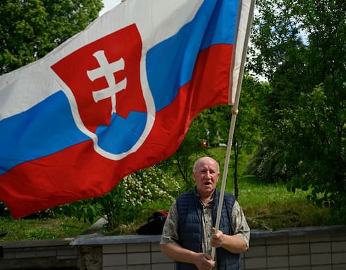 Un hombre reza a fuera del hospital, donde se encuentra Fico con la bandera de Eslovaquia. Fuente: AP